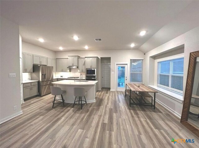 kitchen featuring a center island with sink, gray cabinets, a kitchen bar, and appliances with stainless steel finishes