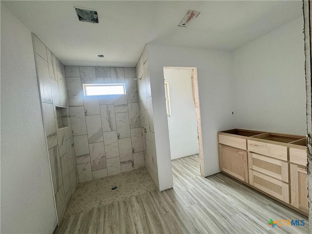 bathroom with wood finished floors and tiled shower