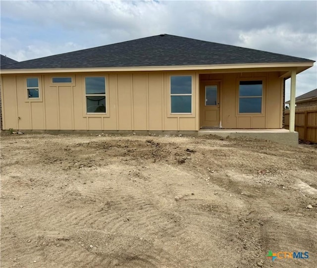 rear view of property featuring fence, board and batten siding, and roof with shingles