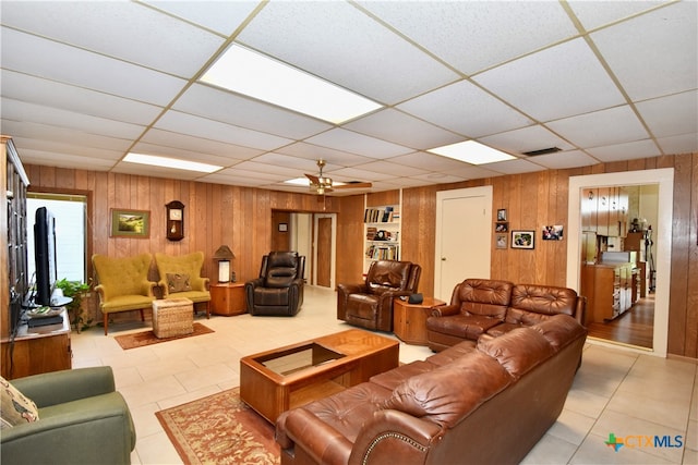 tiled living room with built in shelves, a paneled ceiling, wooden walls, and ceiling fan