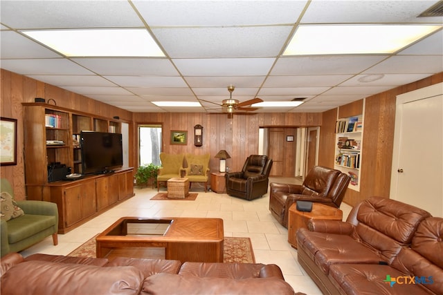 tiled living room with built in shelves, a paneled ceiling, wooden walls, and ceiling fan