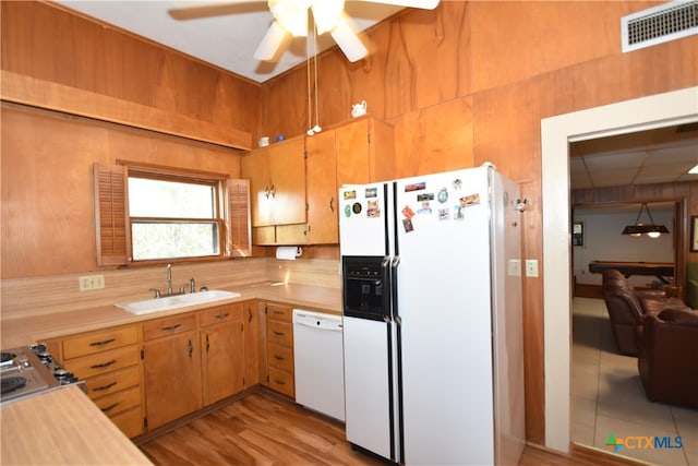 kitchen with light hardwood / wood-style floors, sink, ceiling fan, white appliances, and wooden walls