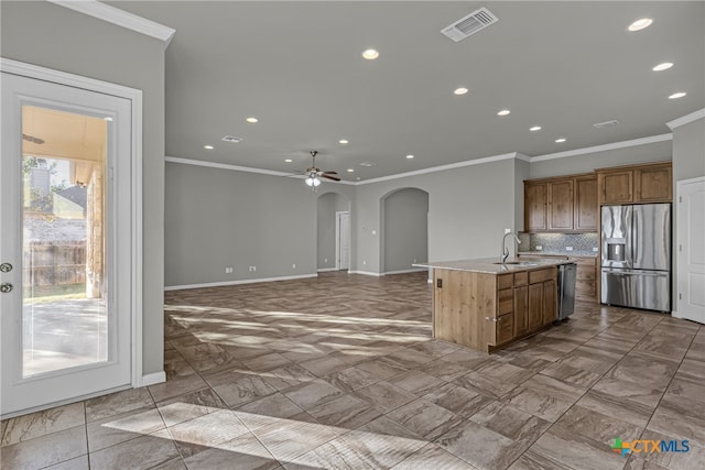 kitchen featuring crown molding, backsplash, appliances with stainless steel finishes, an island with sink, and ceiling fan