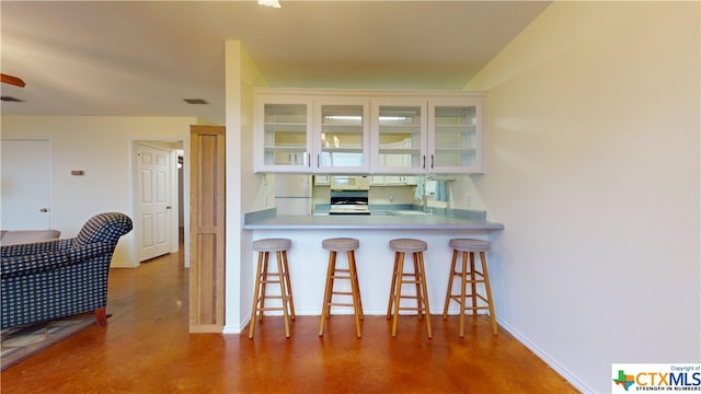 kitchen with a breakfast bar, kitchen peninsula, sink, white appliances, and white cabinetry