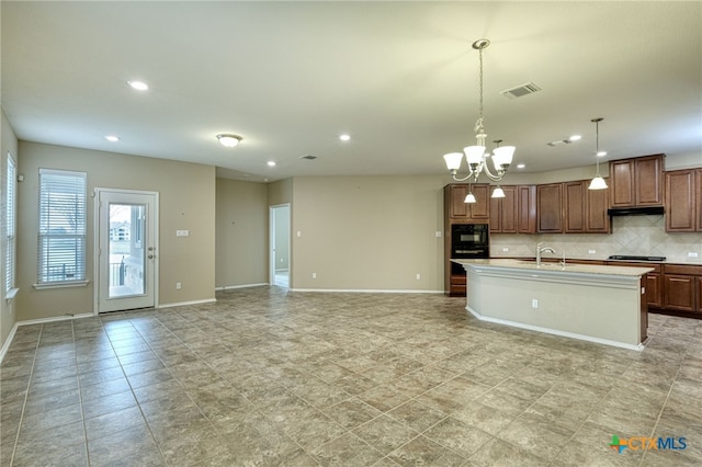 kitchen with pendant lighting, backsplash, a kitchen island with sink, sink, and gas stovetop