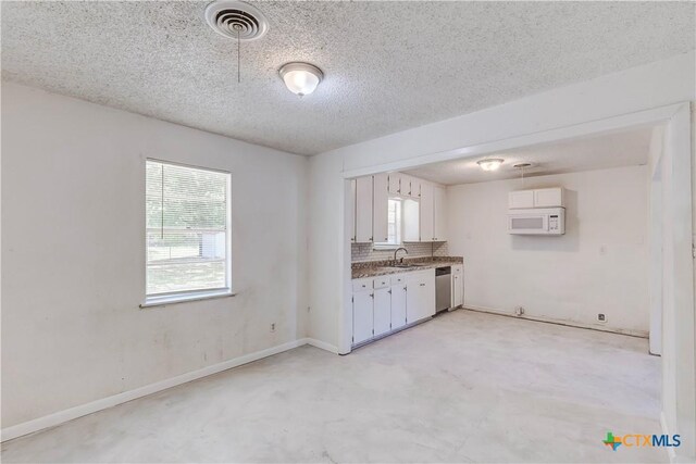 907 Curry Ave, Copperas Cove, TX 76522 - kitchen featuring dishwasher, white microwave, concrete flooring, white cabinets, and a textured ceiling