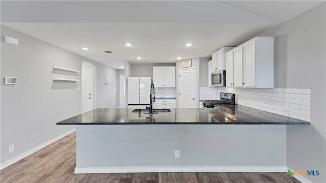 kitchen featuring kitchen peninsula, dark stone countertops, stove, and white cabinetry