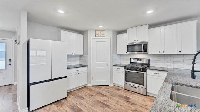 kitchen with light stone countertops, light hardwood / wood-style floors, decorative backsplash, white cabinetry, and appliances with stainless steel finishes