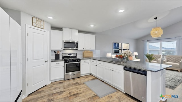 kitchen with decorative light fixtures, lofted ceiling, tasteful backsplash, kitchen peninsula, and appliances with stainless steel finishes