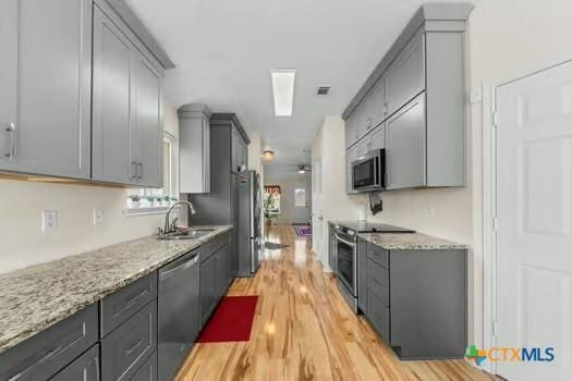 2303 Schwald Rd, Killeen, TX 76543 - kitchen with appliances with stainless steel finishes, gray cabinetry, a sink, light wood-type flooring, and light stone countertops