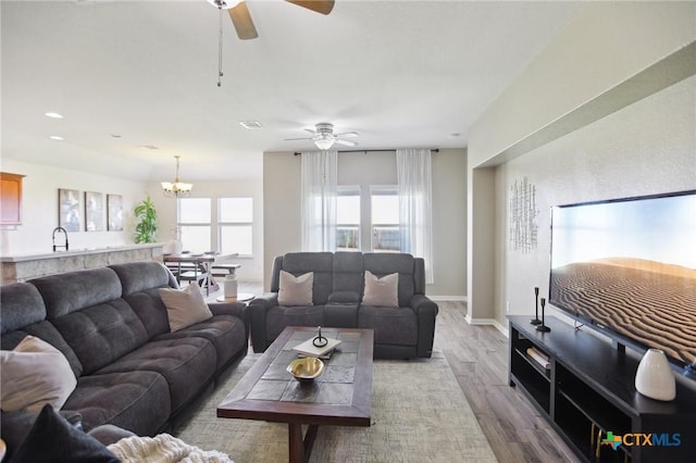 living room with visible vents, baseboards, recessed lighting, ceiling fan with notable chandelier, and light wood-style floors