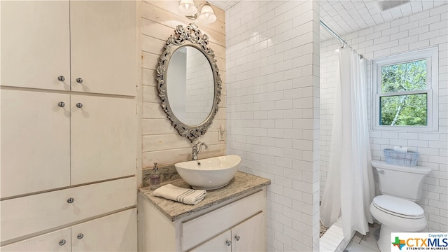 bathroom with walk in shower, vanity, toilet, and tile walls