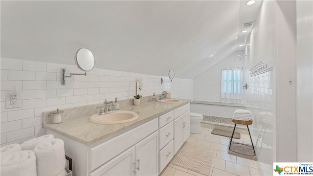 bathroom with toilet, tile patterned floors, vaulted ceiling, tile walls, and vanity