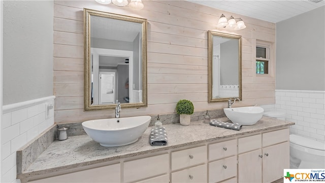 bathroom with toilet, wood walls, vanity, and tile walls