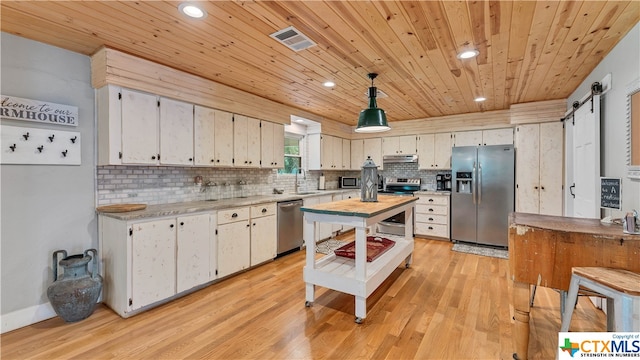 kitchen with stainless steel appliances, white cabinetry, a barn door, hanging light fixtures, and light hardwood / wood-style flooring