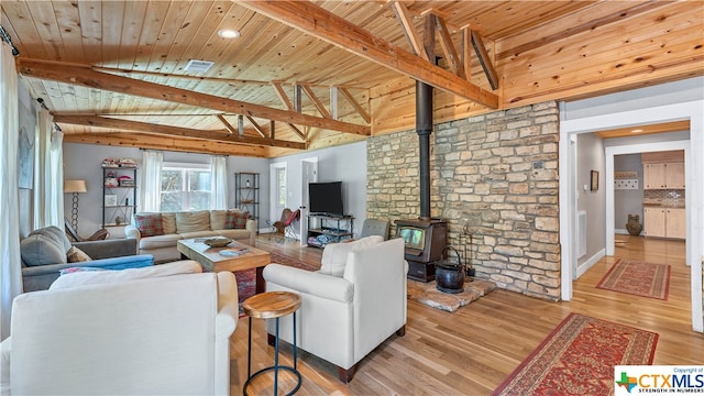 living room featuring lofted ceiling with beams, light wood-type flooring, wood ceiling, and a wood stove