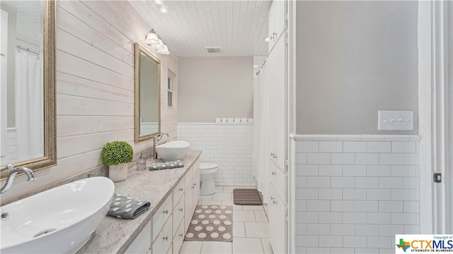 bathroom with tile patterned flooring, curtained shower, vanity, toilet, and tile walls