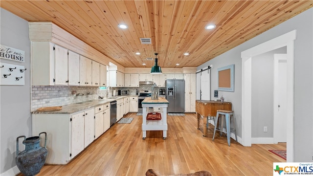 kitchen with a kitchen island, appliances with stainless steel finishes, a barn door, light hardwood / wood-style floors, and white cabinets