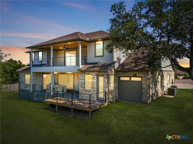 back house at dusk featuring a garage, a balcony, central AC unit, and a yard