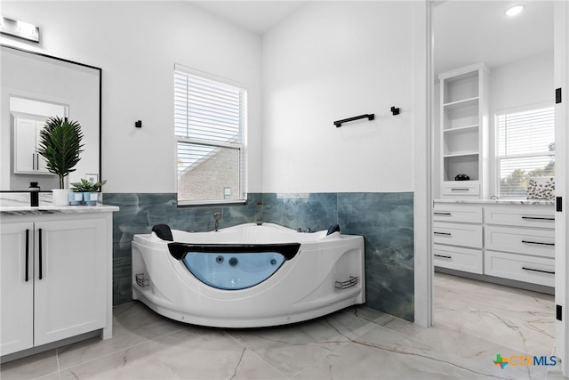 bathroom with plenty of natural light, tile walls, a tub to relax in, and vanity