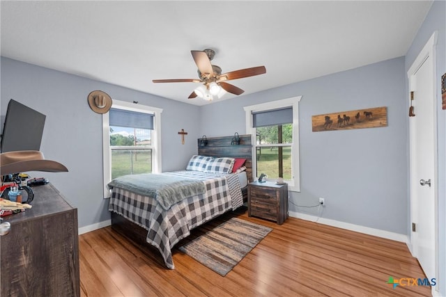 bedroom featuring wood finished floors, baseboards, a ceiling fan, and multiple windows