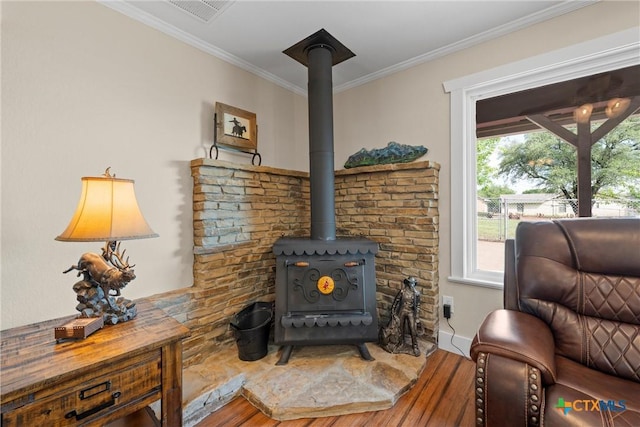 living area featuring wood finished floors, a wood stove, visible vents, ornamental molding, and baseboards