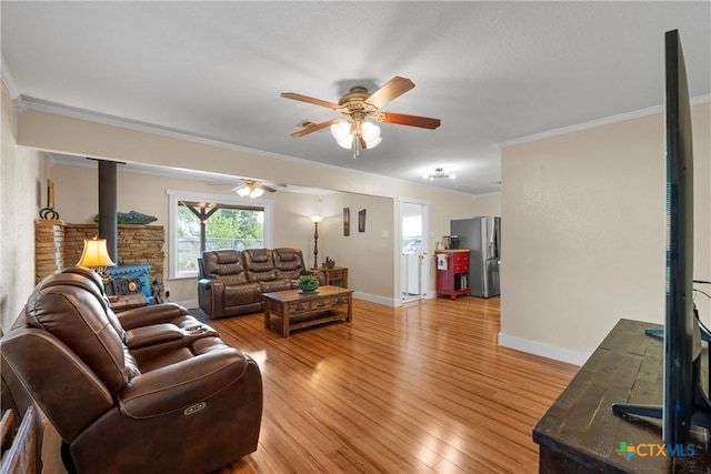 living room with ceiling fan, light wood-style floors, a wood stove, and crown molding