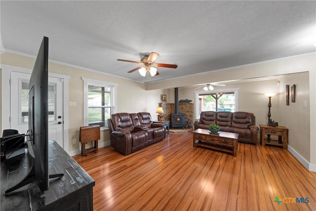 living room with light wood finished floors, ceiling fan, a wood stove, and crown molding