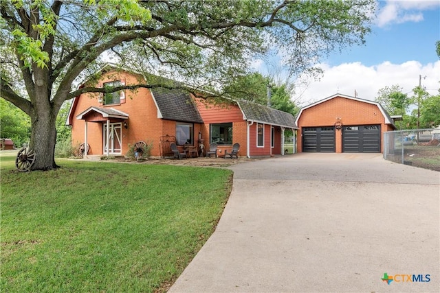 view of front of property with a gambrel roof, a detached garage, a front yard, brick siding, and roof with shingles
