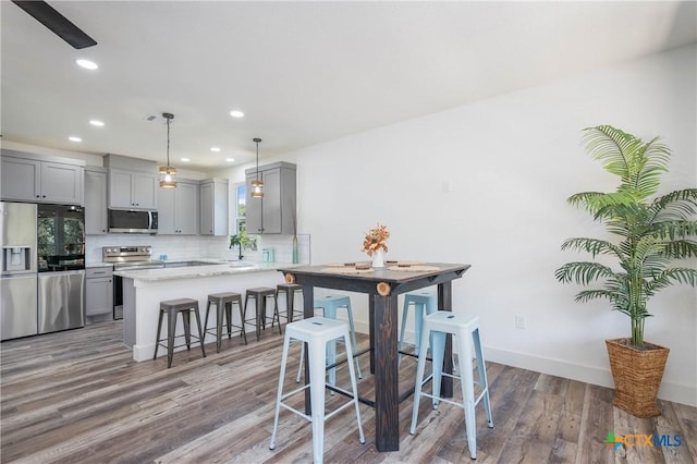 kitchen with tasteful backsplash, appliances with stainless steel finishes, a breakfast bar area, decorative light fixtures, and gray cabinets