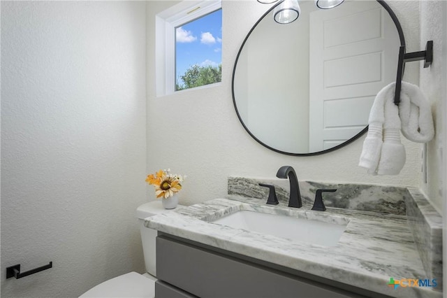 bathroom featuring a textured wall, vanity, and toilet