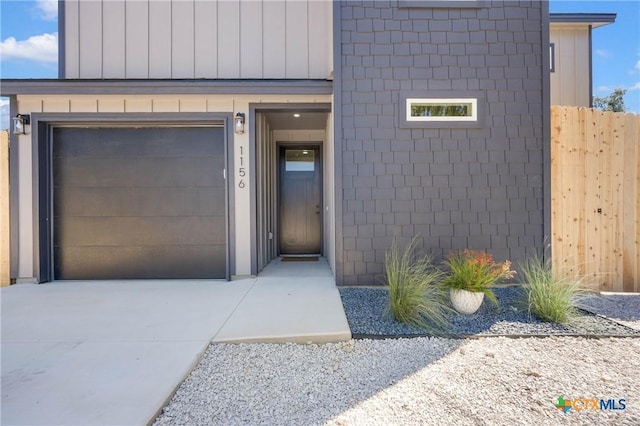 doorway to property with a garage, board and batten siding, fence, and concrete driveway