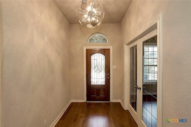 foyer entrance with dark hardwood / wood-style floors, a notable chandelier, and french doors