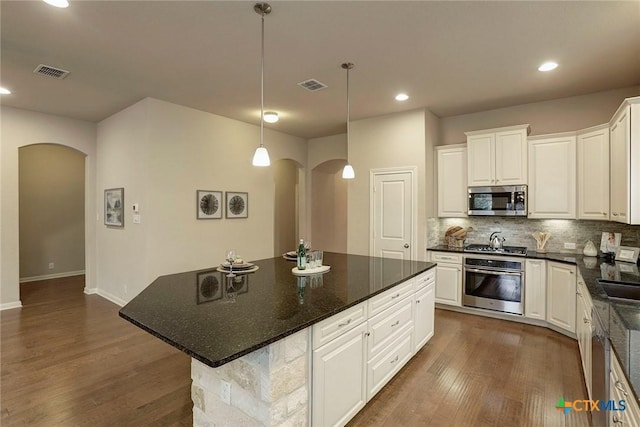 kitchen featuring appliances with stainless steel finishes, a center island, tasteful backsplash, white cabinets, and decorative light fixtures