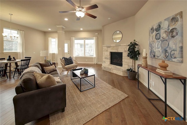 living room with ornate columns, a stone fireplace, ceiling fan with notable chandelier, and dark hardwood / wood-style flooring