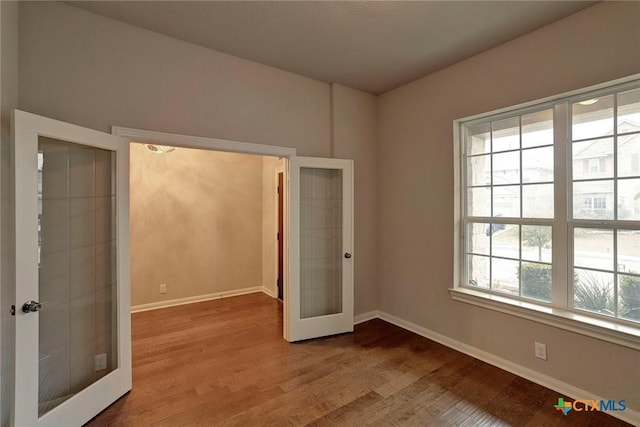 unfurnished bedroom with multiple windows, wood-type flooring, and french doors