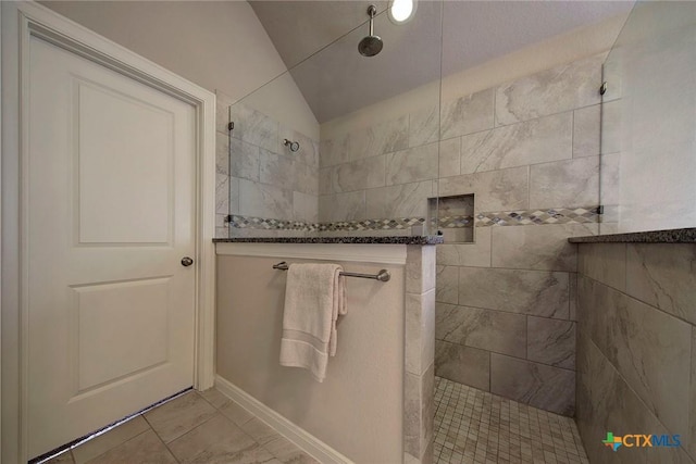 bathroom with a tile shower, tile patterned flooring, and vaulted ceiling