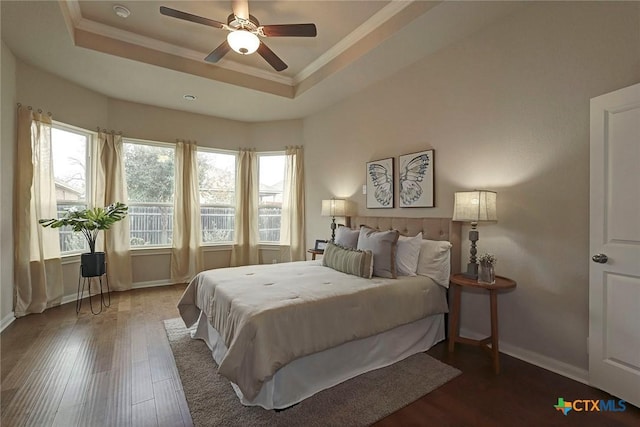 bedroom with crown molding, dark wood-type flooring, a raised ceiling, and ceiling fan