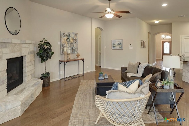 living room featuring dark hardwood / wood-style flooring, a stone fireplace, and ceiling fan