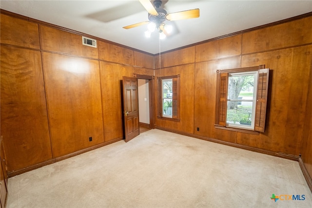 unfurnished bedroom featuring wood walls, ceiling fan, and light colored carpet