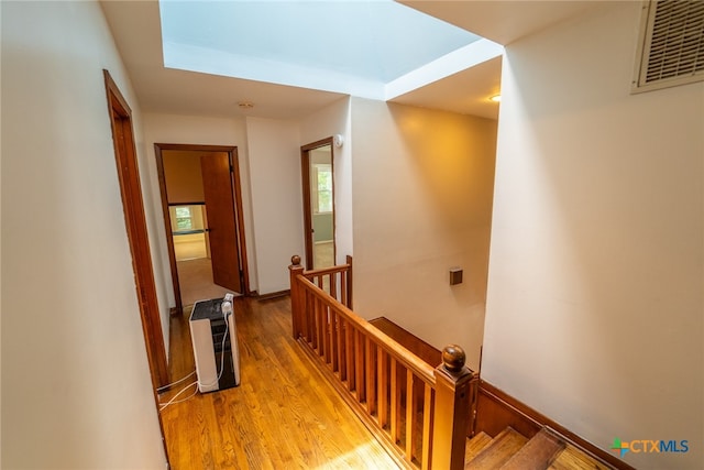 hallway with heating unit, light wood-type flooring, and a skylight