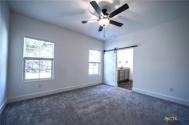 unfurnished bedroom featuring a barn door, ceiling fan, ensuite bathroom, and multiple windows