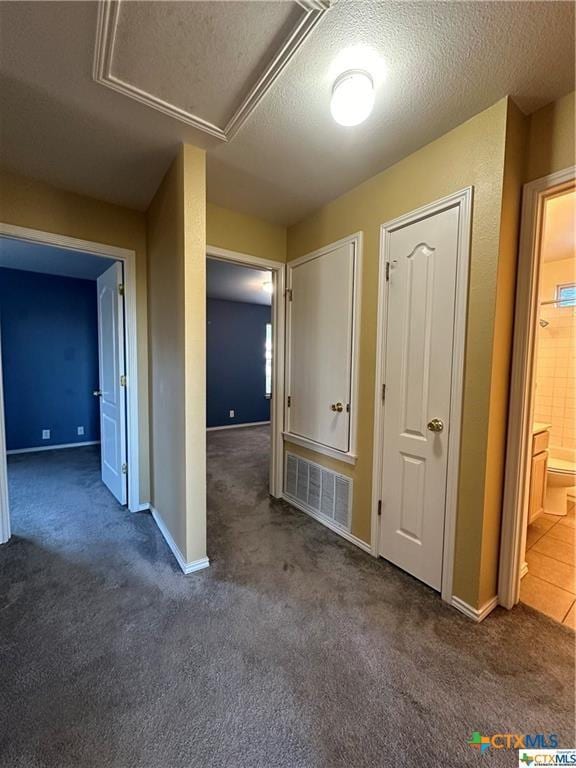 hall featuring baseboards, carpet flooring, visible vents, and a textured ceiling