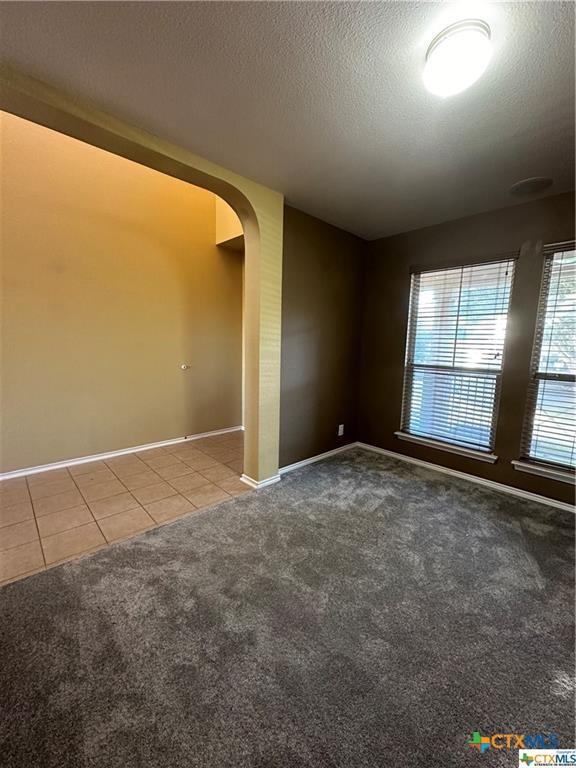 empty room featuring a textured ceiling, carpet, baseboards, tile patterned flooring, and arched walkways