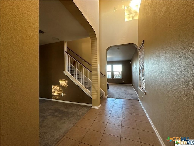 tiled entrance foyer with a textured wall, stairway, baseboards, and carpet floors