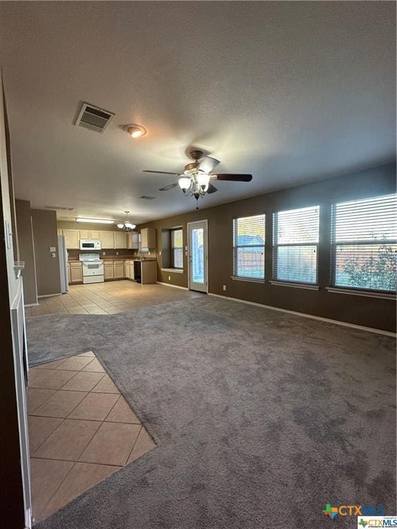 unfurnished living room with a ceiling fan, baseboards, light tile patterned flooring, visible vents, and light colored carpet