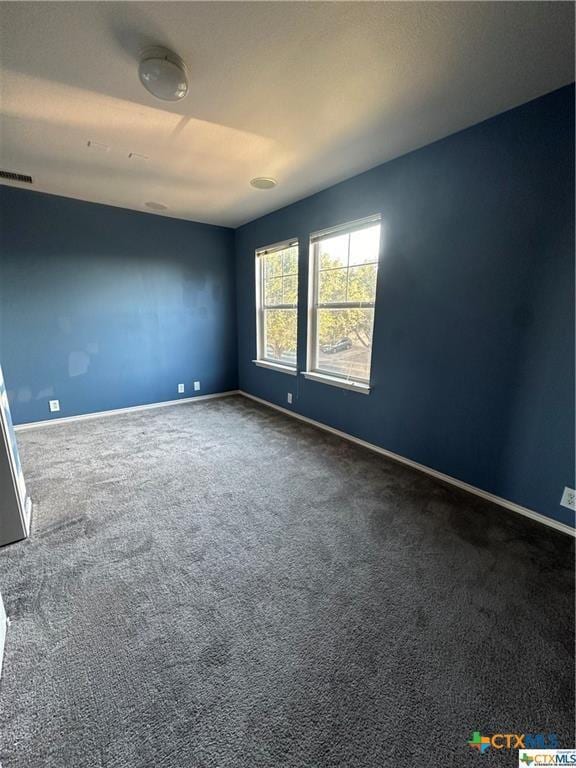 spare room featuring visible vents, baseboards, and dark carpet