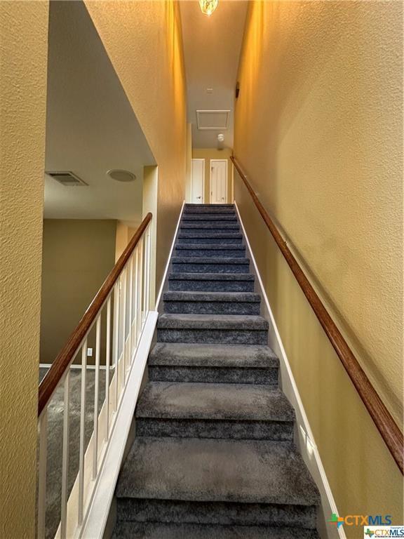 staircase featuring baseboards, visible vents, carpet, and a textured wall