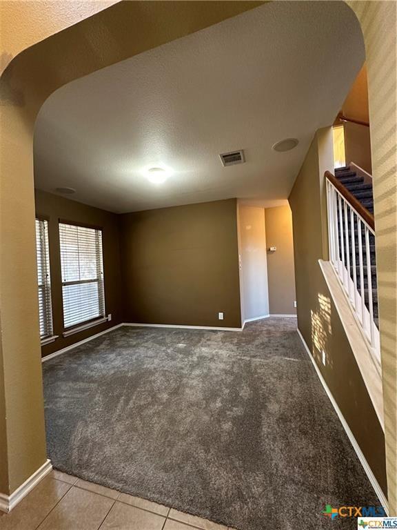 tiled empty room with carpet flooring, visible vents, baseboards, and stairway