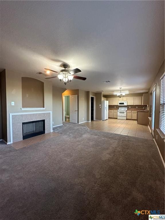 unfurnished living room featuring a ceiling fan, light tile patterned floors, baseboards, a tile fireplace, and light colored carpet
